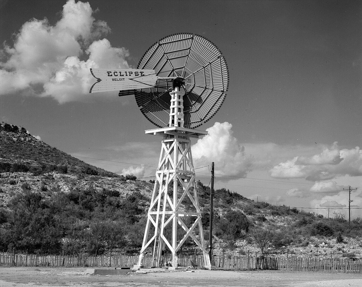 A tall Eclipse windmill standing on open ranch land, in black and white