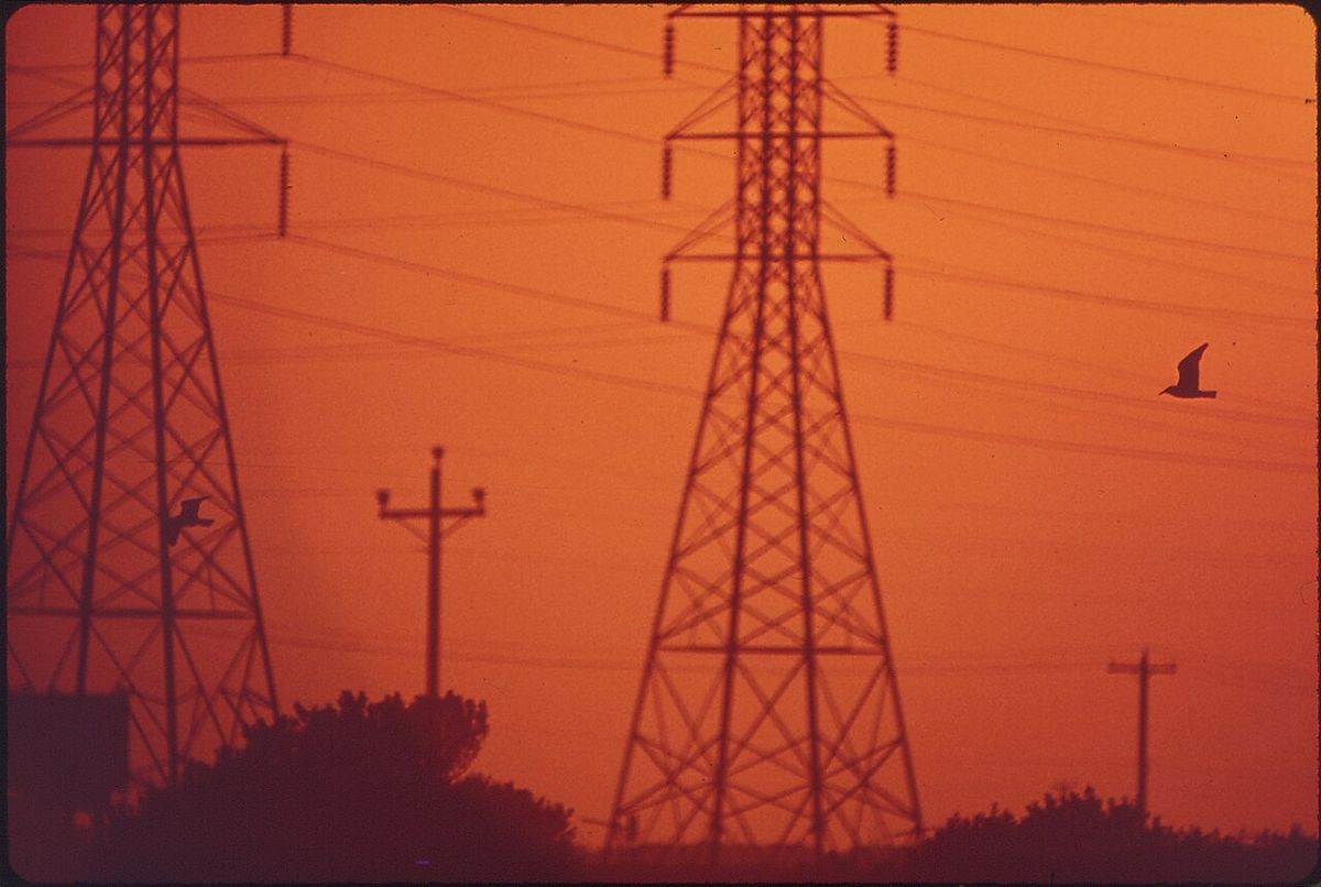 Power lines silhouetted against an orange sunset over an industrial area near Galveston Bay