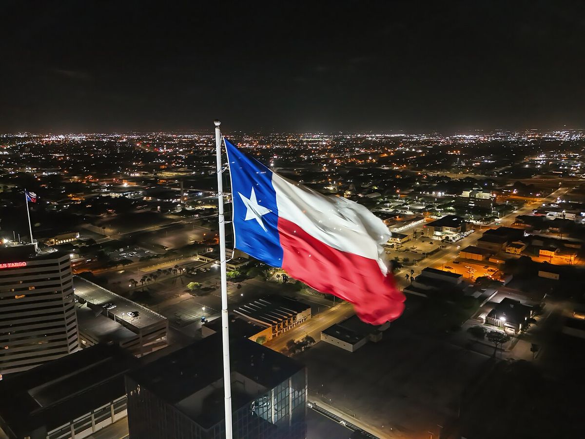 The Texas flag flying at night above the lights of Corpus Christi